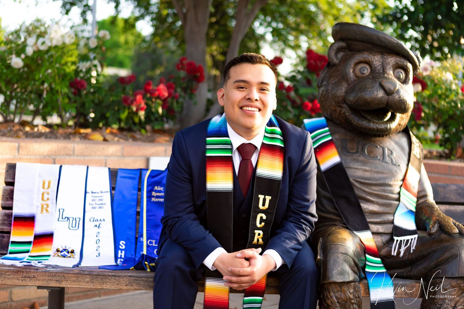 Alex at his UC Riverside graduation, seated beside the campus bear statue